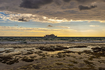 Ferry boat on ocean horizon at sunset with rocky shore