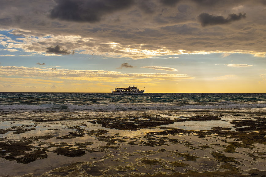 Ferry boat on ocean horizon at sunset with rocky shore
