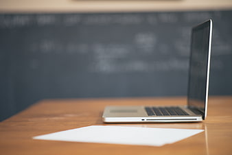 Open Silver Laptop On Wooden Desk With Blurred Chalkboard Background