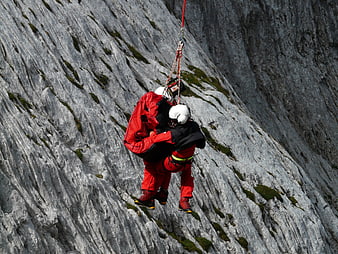 Mountain rescue team abseiling down steep rocky cliff face