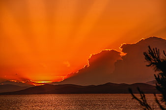 Dramatic Orange Sunset Over Sea With Silhouetted Mountains And Clouds