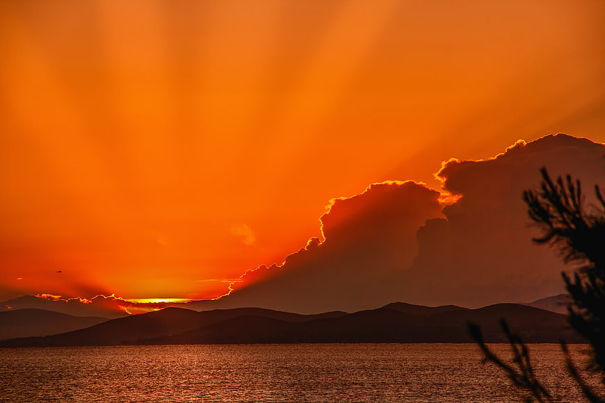 Dramatic Orange Sunset Over Sea With Silhouetted Mountains And Clouds