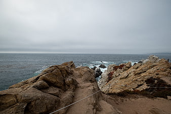 Rocky coastal path with ocean view under overcast sky