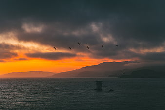 Dramatic Sunset Over Ocean with Birds and Mountains