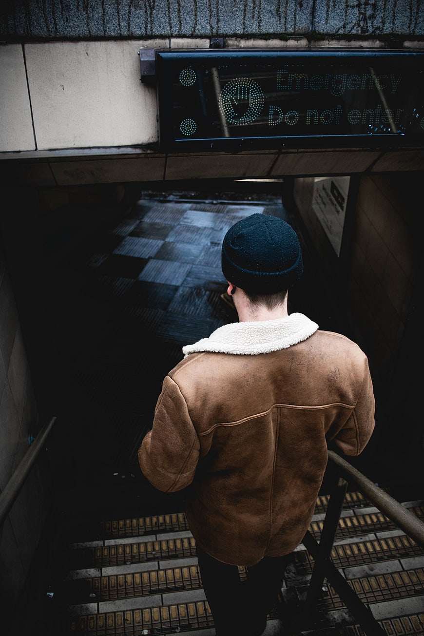 Man in Brown Jacket Descending Dark Subway Stairs
