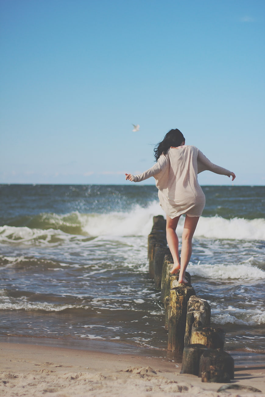 Woman balancing on wooden groynes at the beach
