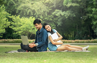 Young Asian couple studying with laptop on grass in park