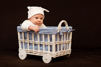 Cute baby in white hat sitting in vintage wicker pram