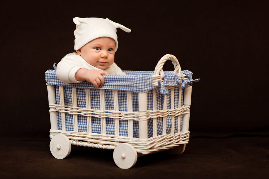 Cute baby in white hat sitting in vintage wicker pram