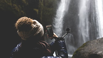 Woman photographing waterfall with smartphone and action camera