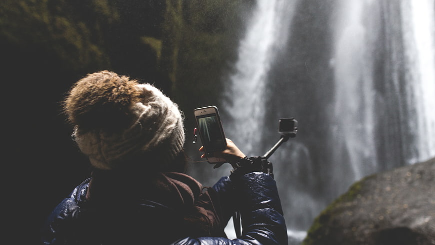 Woman photographing waterfall with smartphone and action camera