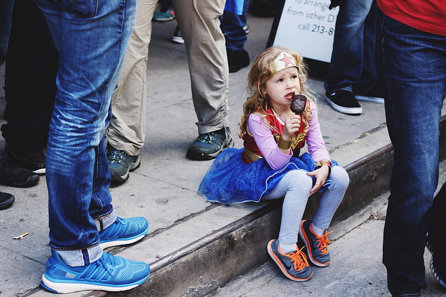Young girl in Wonder Woman costume eating ice cream on city street