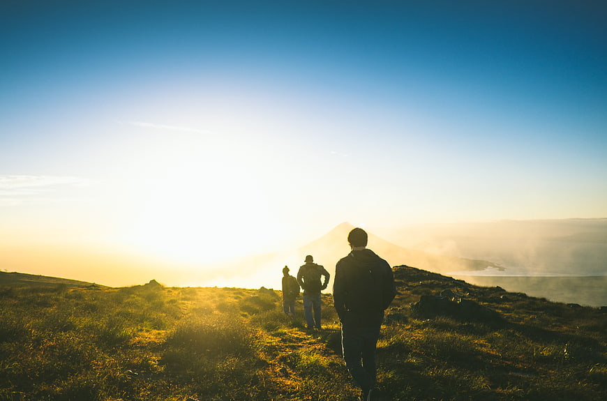 Hikers walking on mountain ridge at sunrise with foggy valley