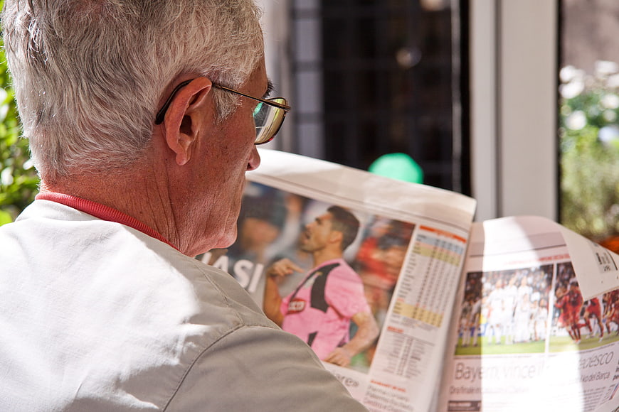 Senior man reading sports newspaper with soccer news