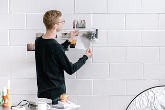 Man pinning photos to white brick wall in creative workspace
