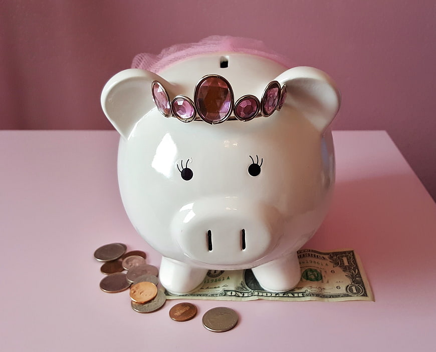 White Piggy Bank with Pink Tiara and Coins on Pink Background