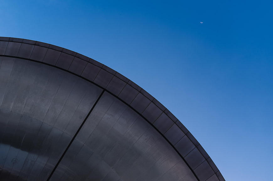 Curved modern building roof against blue sky with crescent moon