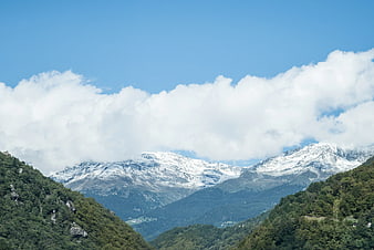 Snow-Capped Mountain Peaks Rising Above Green Forested Hills