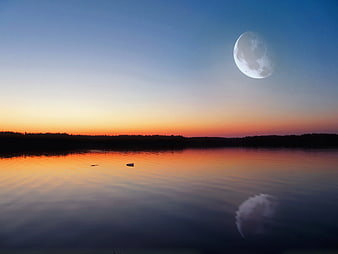 Large moon over calm lake at twilight with sunset reflection