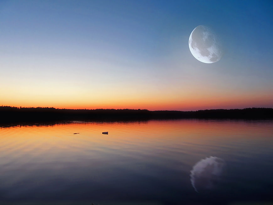 Large moon over calm lake at twilight with sunset reflection