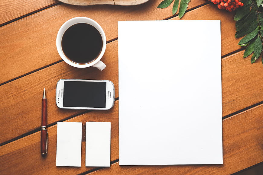 Flat lay of coffee, smartphone, and blank paper on wooden desk