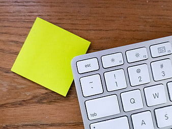 Yellow Sticky Note on Wooden Desk Next to Keyboard