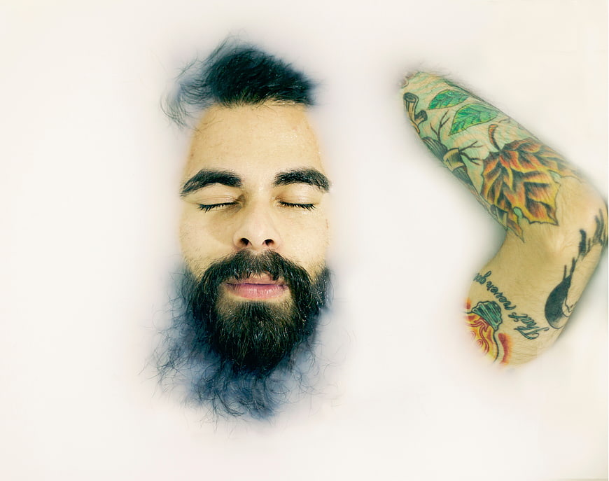 Man with beard and tattoos submerged in white water
