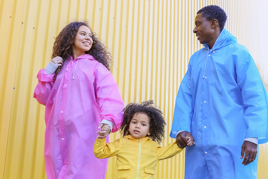Happy Black Family in Colorful Raincoats Against Yellow Wall