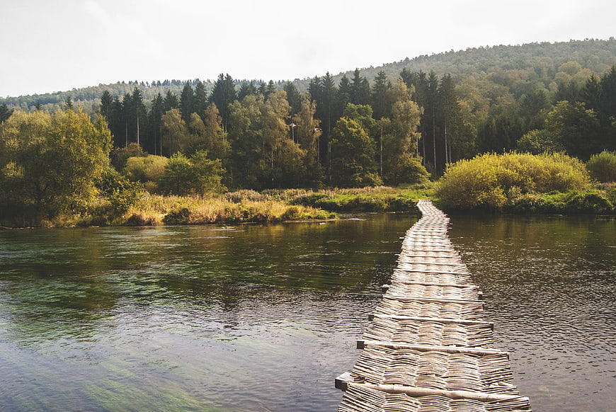 Rustic wooden plank bridge crossing a calm river with forest background