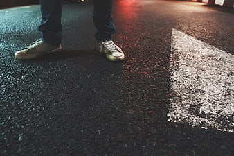 Close-up of worn sneakers on wet asphalt at night