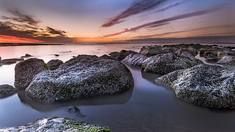 Dramatic Sunset Over Rocky Beach with Smooth Water