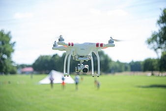 White drone flying over green field with camera