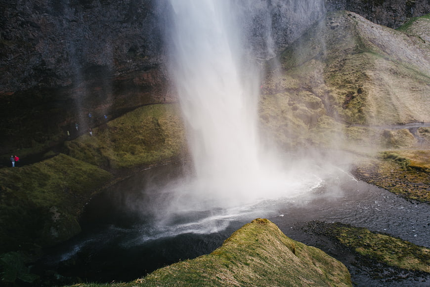 Majestic waterfall cascading into a misty pool with hikers nearby