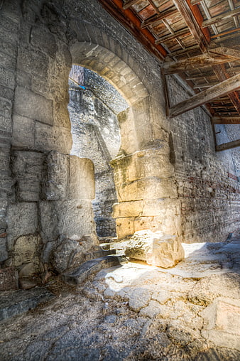 Sunlit stone archway in ancient ruins with wooden ceiling
