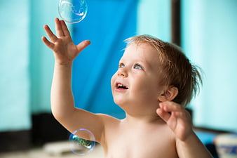 Toddler boy reaching for floating soap bubbles indoors