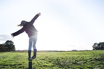 Woman balancing on post in green field with sun flare