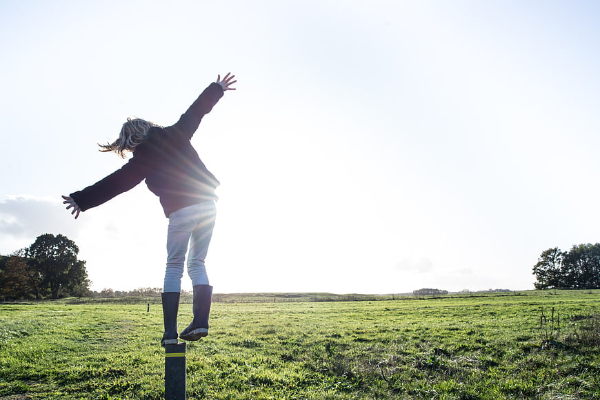 Woman balancing on post in green field with sun flare