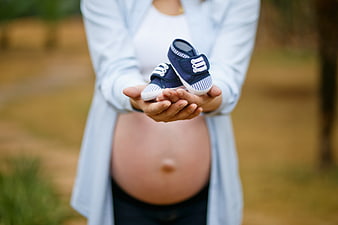 Pregnant Woman Holding Baby Shoes in Park