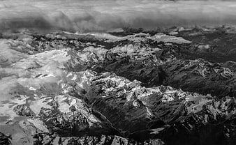 Black and white aerial view of snow-capped mountain peaks through clouds