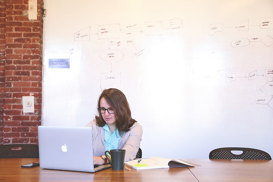 Woman working on laptop in office with whiteboard