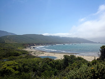 Scenic coastal landscape with sandy beach, ocean waves, and green hills