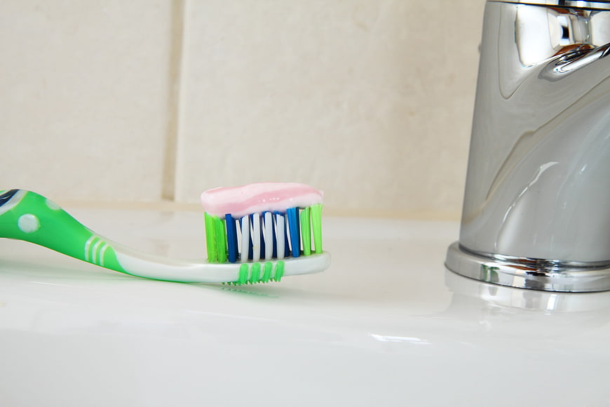 Green Toothbrush With Pink Toothpaste On White Bathroom Sink