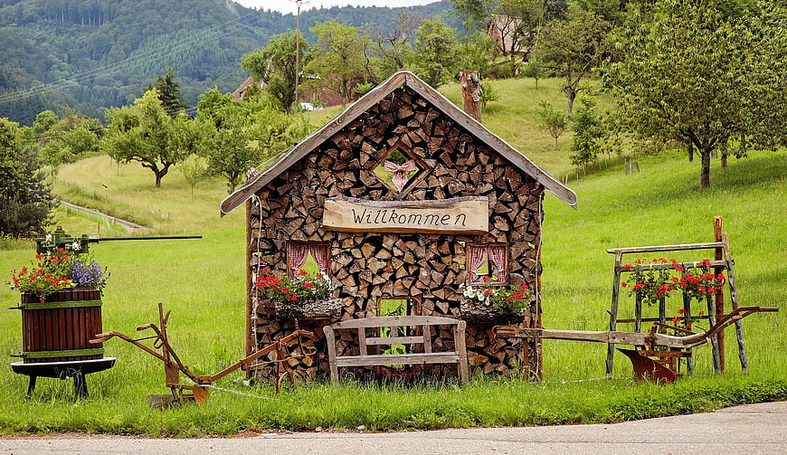 Rustic Firewood Stack House with Welcome Sign in Green Meadow