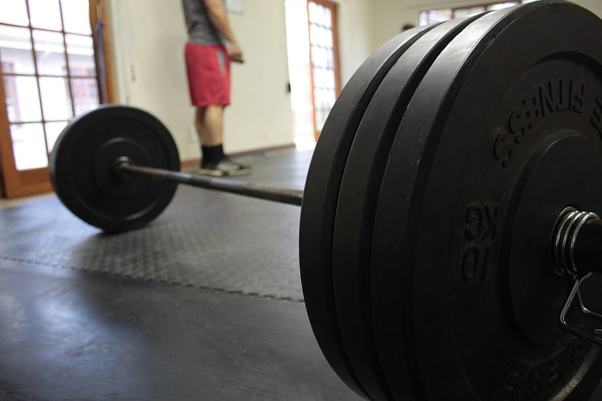 Close-up of a loaded barbell on a gym floor with a blurred athlete in the background