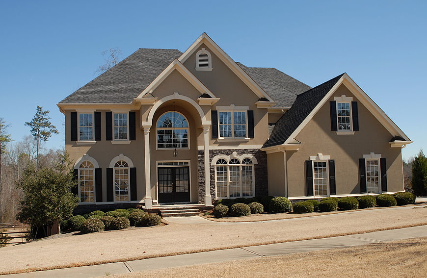 Large beige suburban house with black shutters and blue sky
