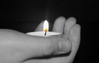 Hand holding a lit tea light candle in the dark