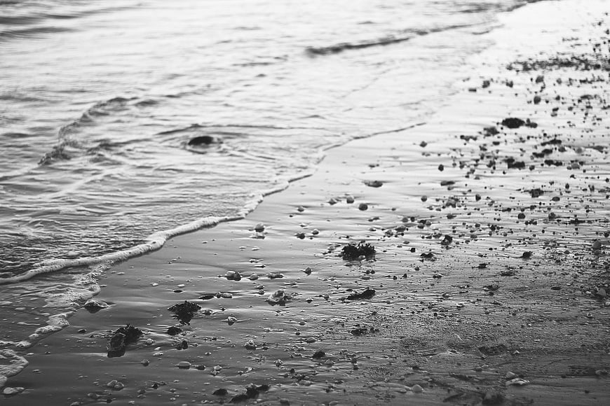 Black and white beach shoreline with gentle waves and pebbles