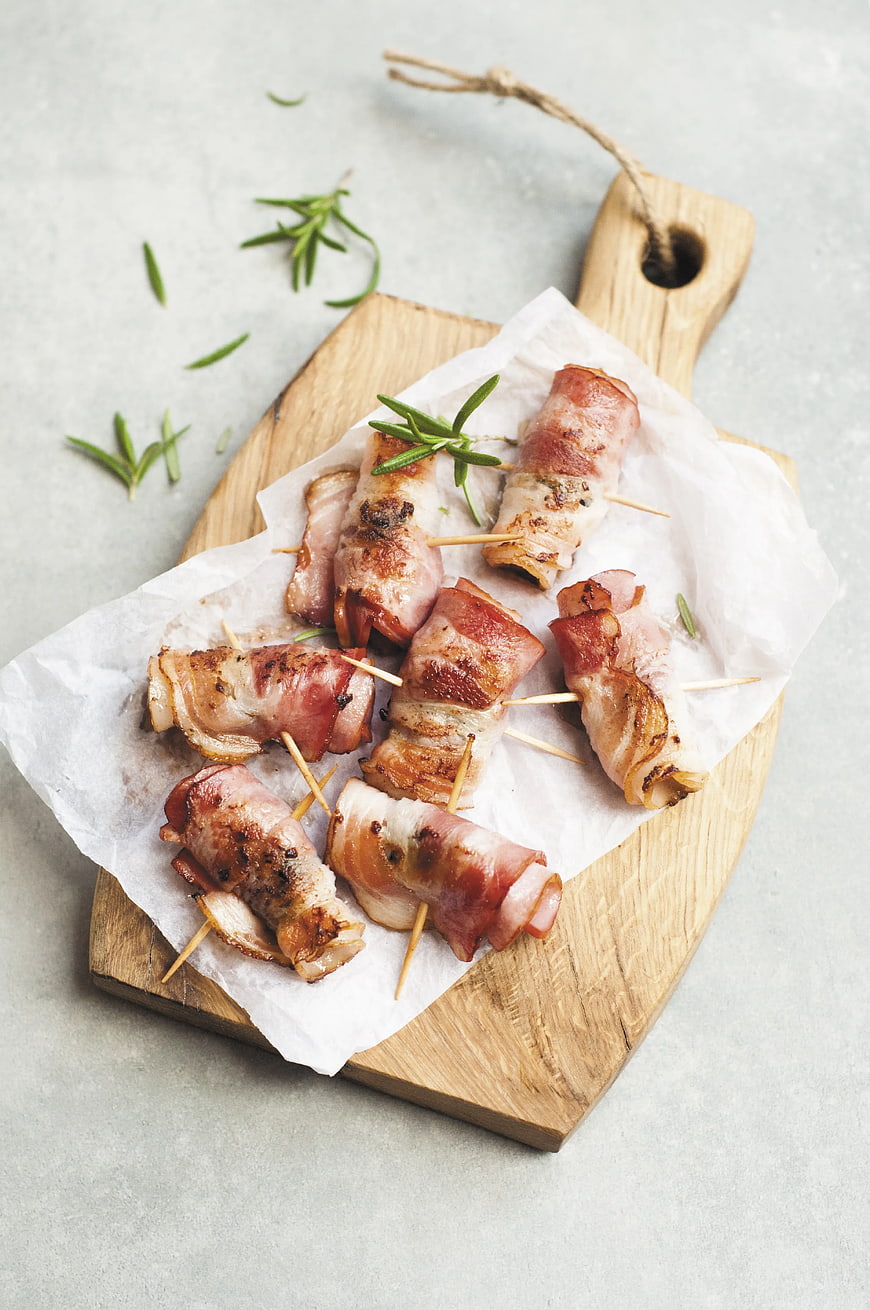 Bacon-wrapped appetizers on wooden board with rosemary
