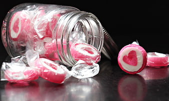 Pink heart candies spilling from glass jar on black background