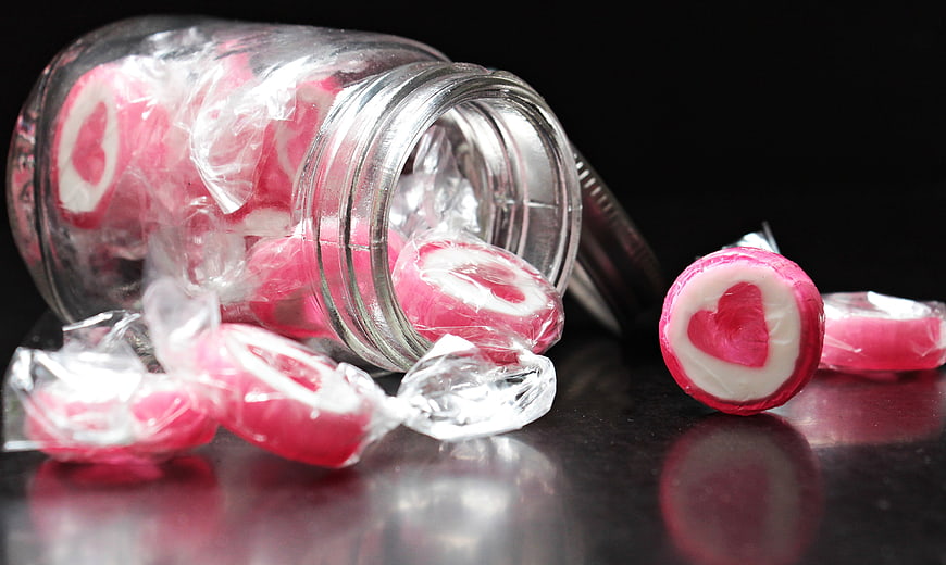 Pink heart candies spilling from glass jar on black background